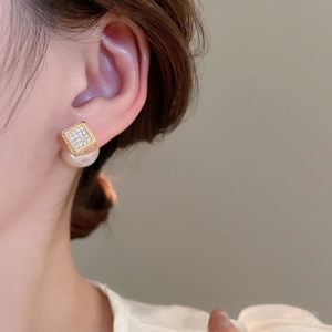 Detail of luxury gold square zircon and pearl earrings worn for a French elegant look