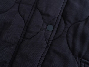 Close-up of wavy quilted fabric and matte black snap button on the padded jacket