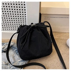 Detail of black nylon drawstring bucket bag with adjustable strap and side brand label