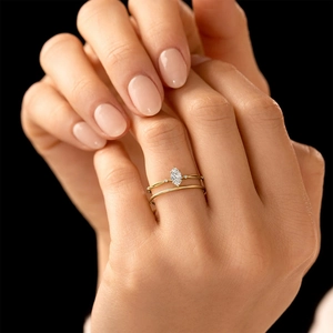 Dettaglio di un anello con diamante marquise e doppia fascia in oro sulla mano di una modella