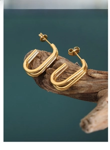 Detail of gold geometric U-shaped double-hoop earrings on natural wood texture