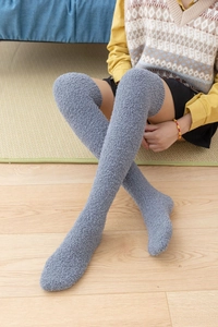 Thick grey coral fleece over-knee socks worn by a model in a cozy indoor setting