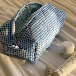 Close-up of quilted plaid cosmetic bag with blue floral lining on white bedding