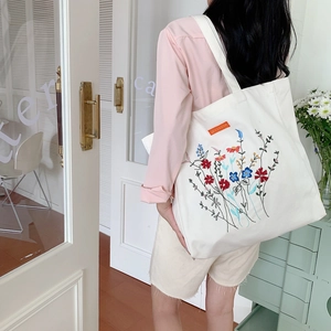 Off-white canvas tote bag featuring vibrant floral embroidery and a spacious interior