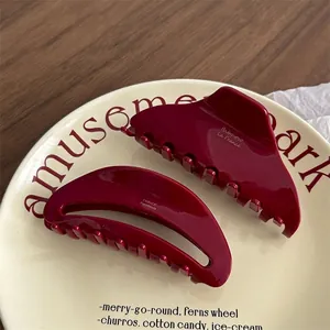 Deep red acetate hair claws with gold lettering on a vintage ceramic plate in French style