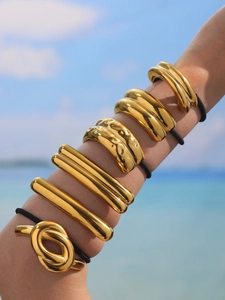 Close-up of golden metallic hair ties in various textures on wrist with ocean background