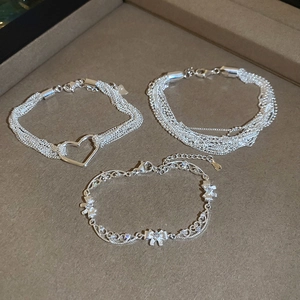 Detailed view of layered silver bracelets with heart and bow pendants on a tray