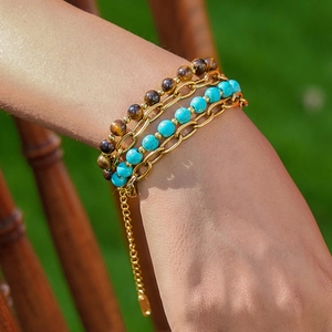 Layered gold chain bracelet with tiger eye and turquoise beads on a woman's wrist