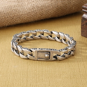 Macro detail of vintage silver Cuban chain bracelet with ornate floral engravings and clasp