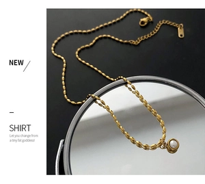 Macro detail of a gold chain necklace with a purple pearl pendant on a dark mirror