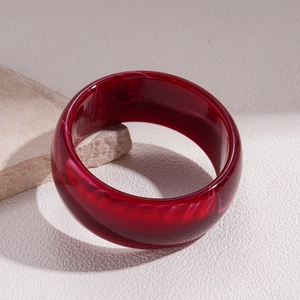 Close-up of deep red resin bangle with marble texture on a natural stone base
