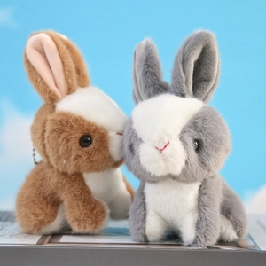 Cute plush rabbit keychains in brown and grey sitting against a blue sky background