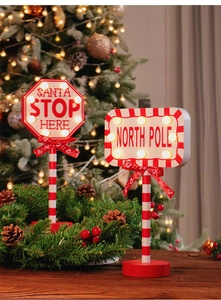 Detail of wooden Santa Stop Here LED road sign with candy cane pole and festive lights