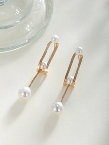 Macro detail of gold plated oval earrings with white pearls and minimalist geometric lines
