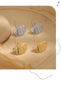 Détail de boucles d'oreilles feuille de ginkgo texturées en or et argent sur fond chaud