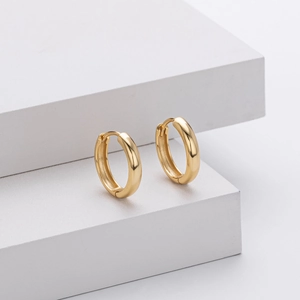 Detailed view of polished golden s925 silver hoop earrings on white stone block