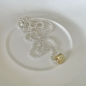 Close-up of dual-tone 925 silver beaded chain with a golden cylindrical pendant on a dish