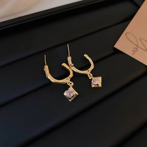 Detail of gold C-shaped earrings featuring pink heart-shaped cubic zirconia on black leather