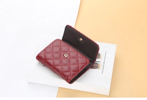 Detail of burgundy quilted leather card holder with gold snap button on a white book