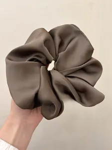 Close-up of oversized dark brown satin scrunchie with silk-like pleated texture detail