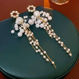 Detail showing clusters of white pearls with long gold chain tassels on floral earrings