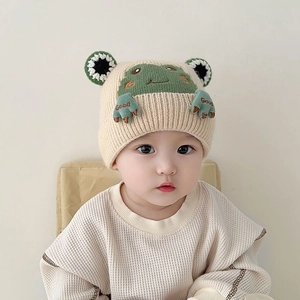 Cute beige baby knitted winter hat with green frog character and warm ear flaps