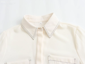 Close-up of cream shirt neckline featuring black contrast stitching and size S label