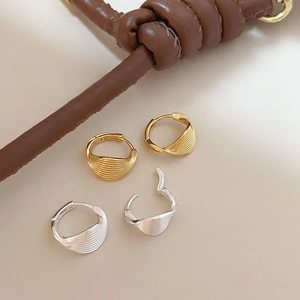 Detailed view of gold and silver twisted hoop earrings on a minimalist beige background