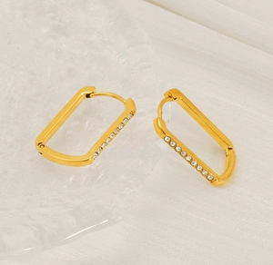 Close-up of gold U-shaped earrings with micro-inlaid zircons on a white silk background