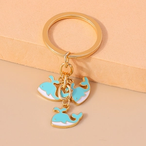 Détail d'un porte-clés doré avec trois pendentifs baleines bleu et blanc sur un socle doux