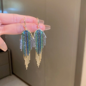 Detail of long fringe earrings with blue and green rhinestones and golden chain tassels