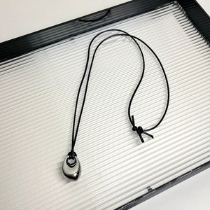 Close-up of black onyx beaded necklace with silver teardrop pendant on textured tray
