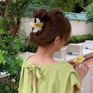 Tropical Plumeria flower hair claw clip worn by a model in a summer garden setting