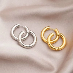 Close-up of polished gold and silver titanium steel hoop earrings on beige silk fabric
