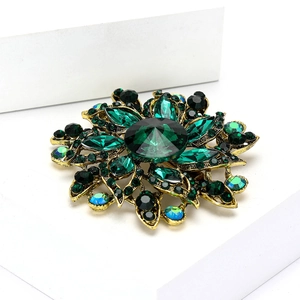 Detailed view of vintage gold brooch with emerald green rhinestones on white block