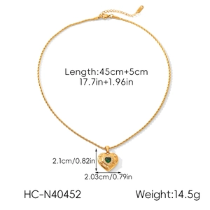 Close-up of golden heart pendant necklace with green center gem and detailed twist chain