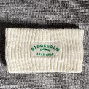 Detailaufnahme von cremeweißem Strickstirnband mit grüner Stockholm-Schweden-Stickerei