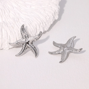 Détail macro de boucles d'oreilles étoile de mer en acier argenté texturé sur corail