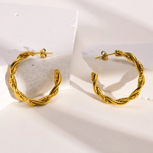 Detail of twisted gold C-shaped hoop earrings on stone with elegant side lighting