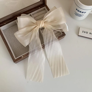 Close-up of beige sheer fabric ribbon bow hair clip on a wooden jewelry box accessory