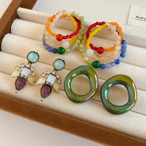 Close-up of vintage glass flower earrings and colorful beaded rings on a velvet tray
