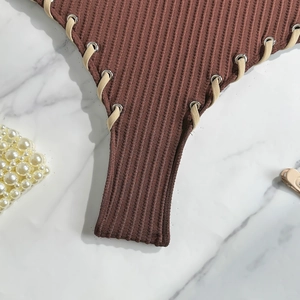 Macro shot of brown ribbed knit swimwear with silver eyelets and cream lace-up detail