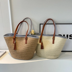 Minimalist woven straw tote bag with brown leather handles and decorative tassel detail