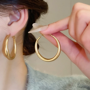 Macro detail of large C-shaped matte gold hoop earrings showcasing the satin metal texture