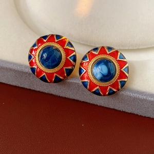 Detail of vintage gold round earrings with red enamel starburst and blue stone