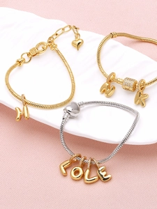 Close-up of gold and silver snake chain bracelets with heart and letter charms