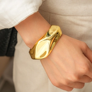 Close-up of a wide gold-colored irregular liquid metal textured bangle on a model wrist