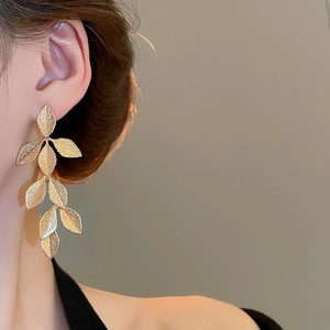 Detail of elegant gold layered leaf tassel earrings worn on ear with soft lighting