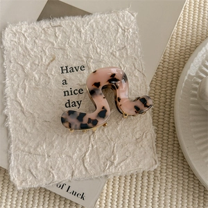 Close-up of pink tortoise acetate hair claw clip with golden metal teeth on soft background