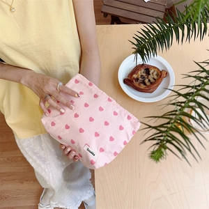 Close-up of pink heart-printed cotton clutch bag with zipper and brand label on a table